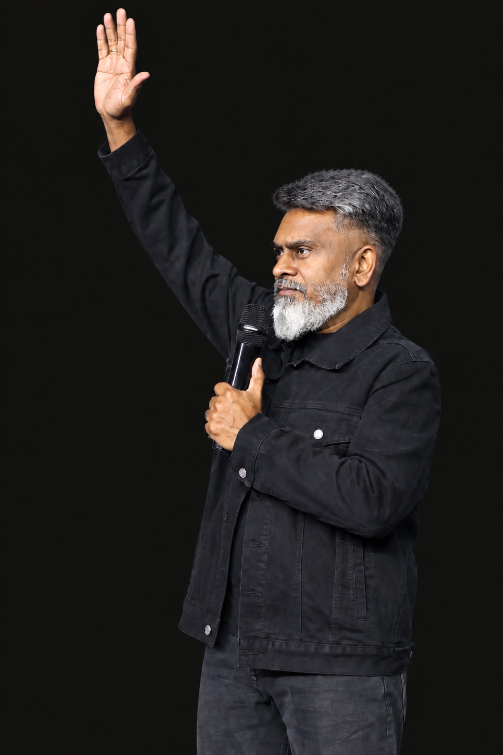 Rev. John holding a microphone with one hand raised.